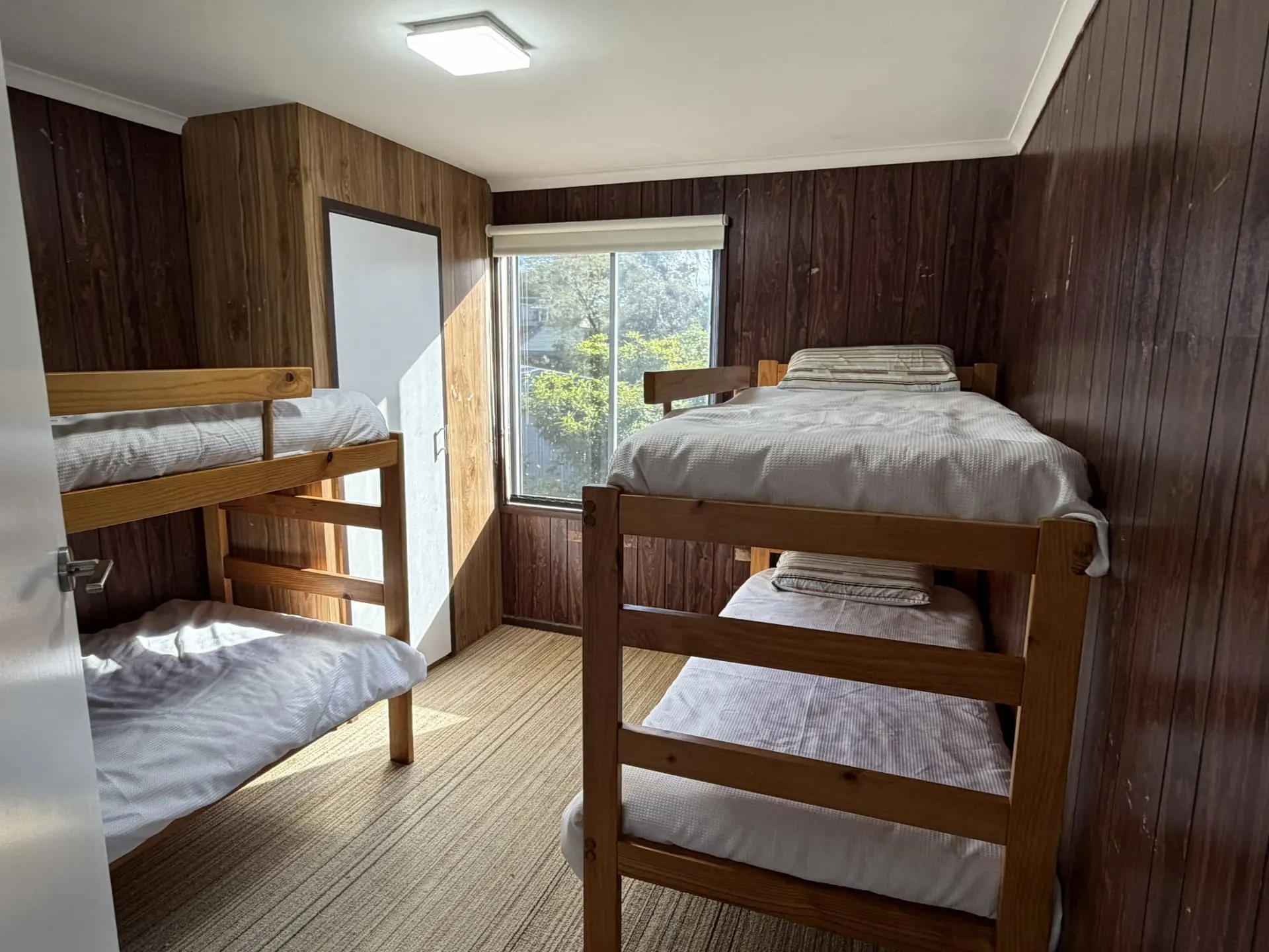 Upstairs bedroom with two timber bunk-bed frames, each with two made-up beds, beside a window and a built-in wardrobe